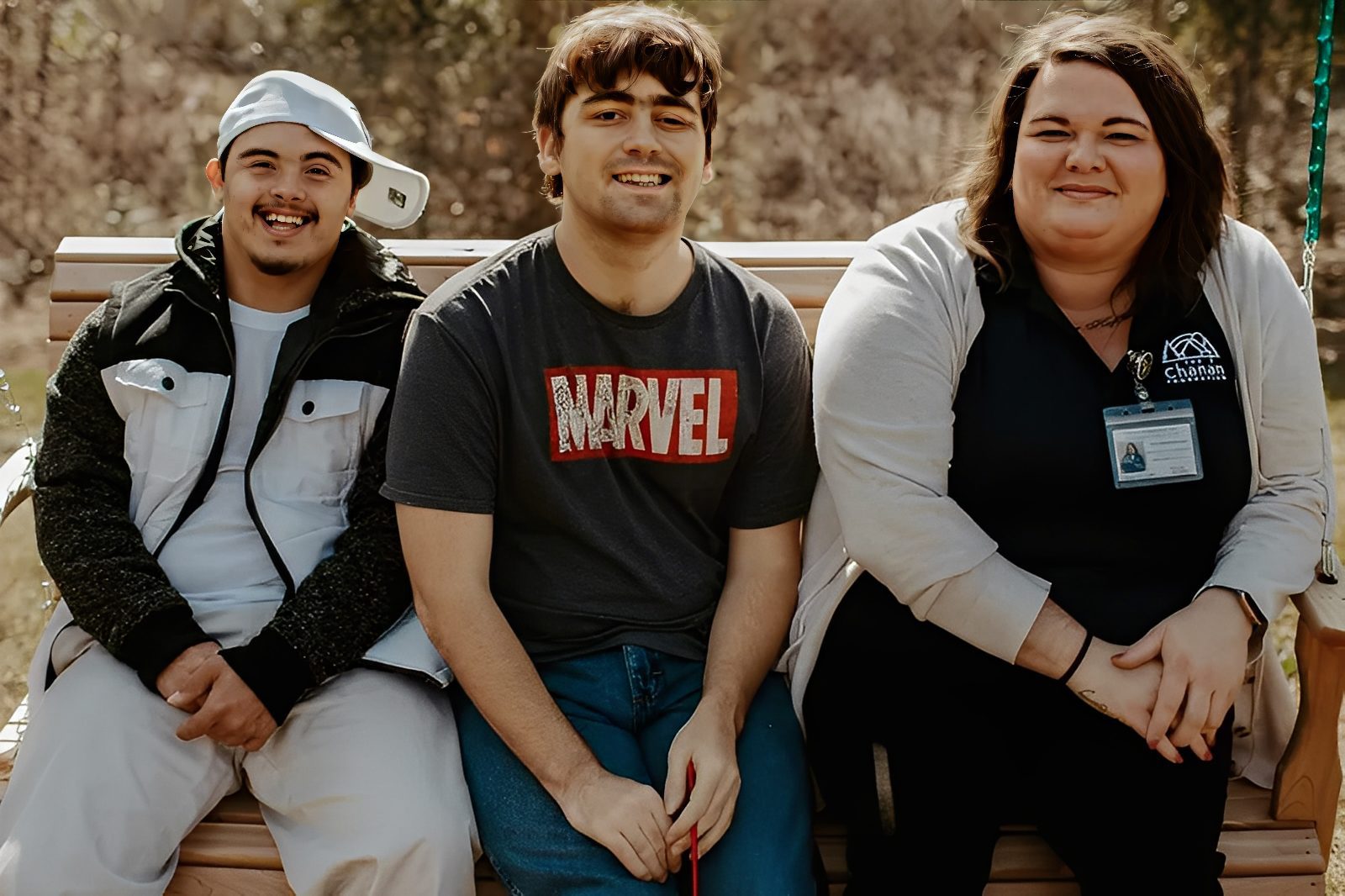 Three people smiling on a wooden bench.