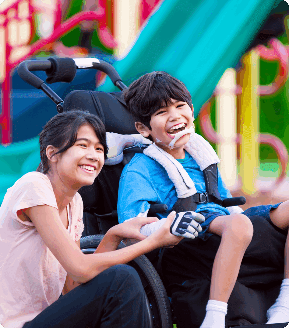 Smiling siblings at playground, wheelchair present.